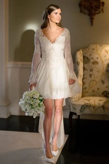 Bride in a short lace wedding dress holding a bouquet indoors.