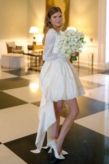 Bride in a short white wedding dress holding a bouquet in an elegant room.