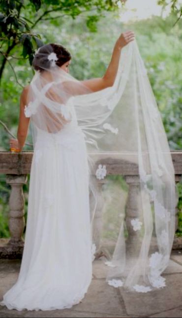 Bride in a white gown holding a flowing veil outdoors.