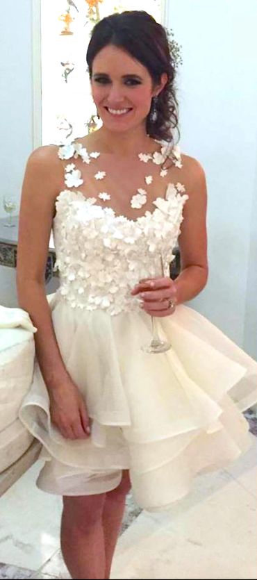 Woman in a white floral dress holding a wine glass, smiling.