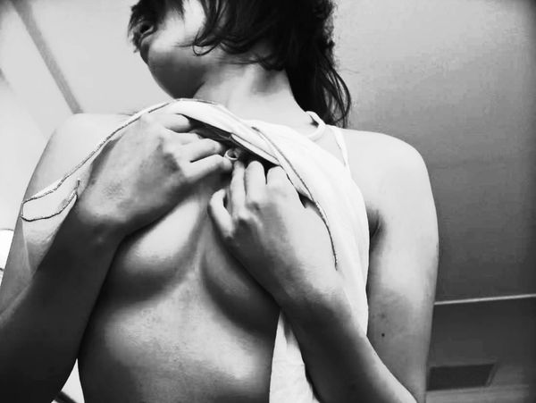 A black and white photograph showing a partial view of a human upper body, with hands holding fabric