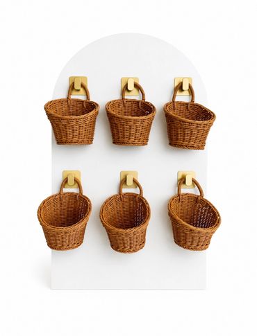 Six wicker baskets hanging on golden hooks against a white backdrop.