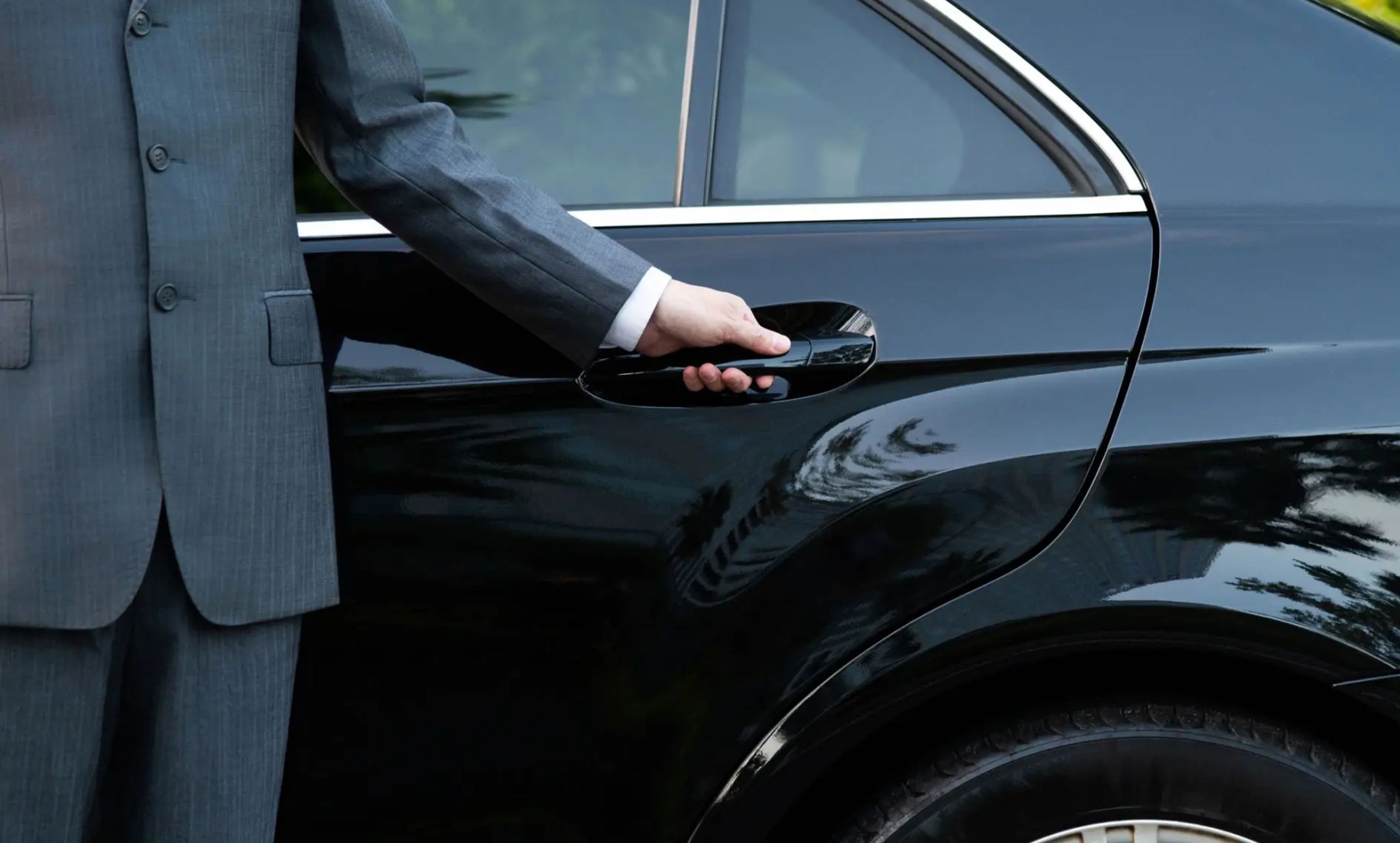 A person in a suit is opening a black car door.