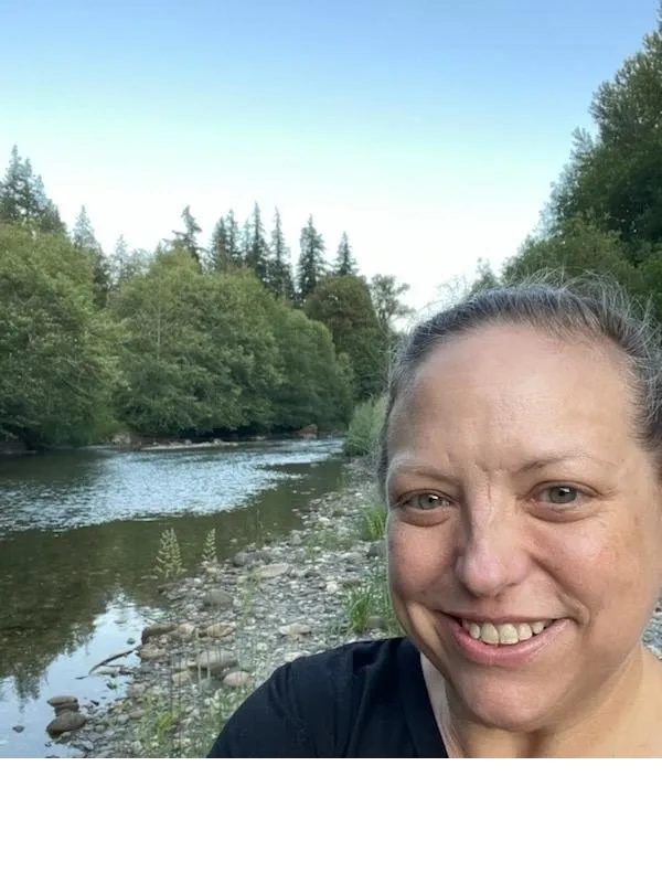 Woman taking a selfie by a peaceful river surrounded by trees.