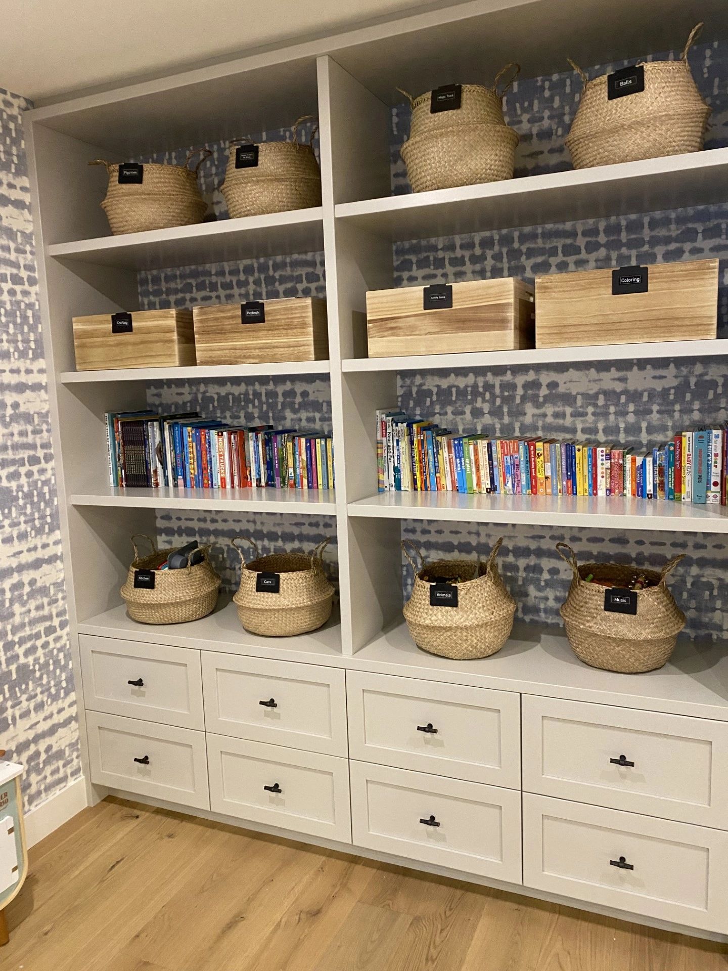 Organized shelves with labeled baskets and books against patterned wall.