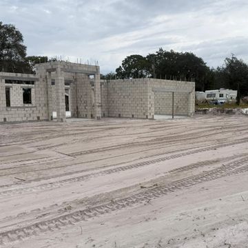 Unfinished block house with tire tracks on sandy soil on a cloudy day.