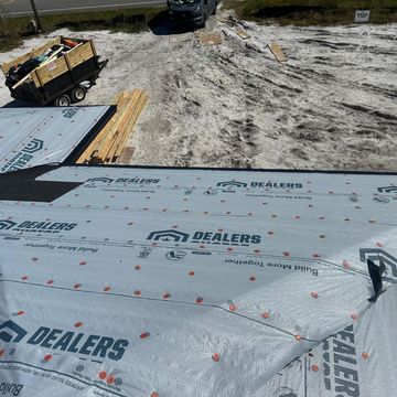 Roof under construction with protective wrap and construction materials on site.