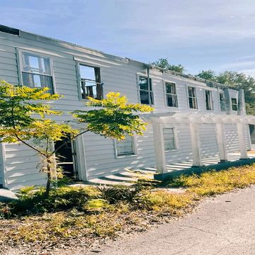 Abandoned white two-story building with broken windows under a clear sky.