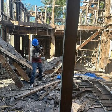 Worker in blue helmet demolishing an old wooden building.