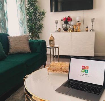 Modern living room with green sofa and laptop on white and gold table.