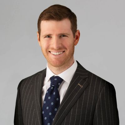 Professional man in pinstripe suit and patterned tie smiling against a gray background.