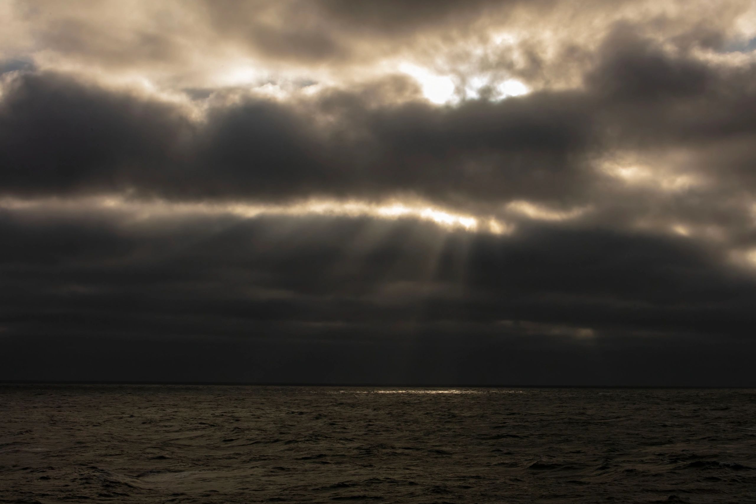 A dark sunset with the light just peeking through clouds over ocean waves.
