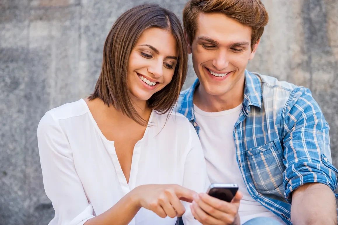 A happy couple smiling while looking at a smartphone together.