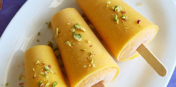 Three mango popsicles garnished with crushed pistachios on a white plate.