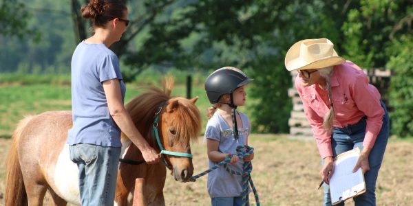 Child learning to ride a pony with adult help and instructor guidance.