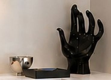 Black mannequin hand sculpture next to a silver cup and black device.