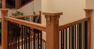 Wooden staircase railing with black metal balusters.