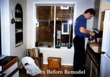 Man working in a dated kitchen with a baby in a rocker.