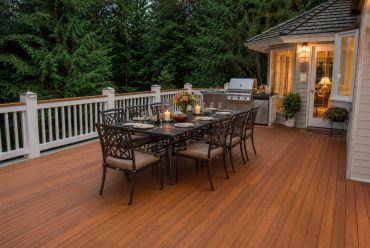 Outdoor dining area on a wooden deck with a grill and candlelit table.