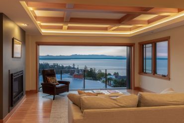 Cozy living room with large windows overlooking a scenic water and mountain view.
