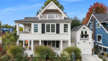 White house with a small porch and a balcony under a blue sky.