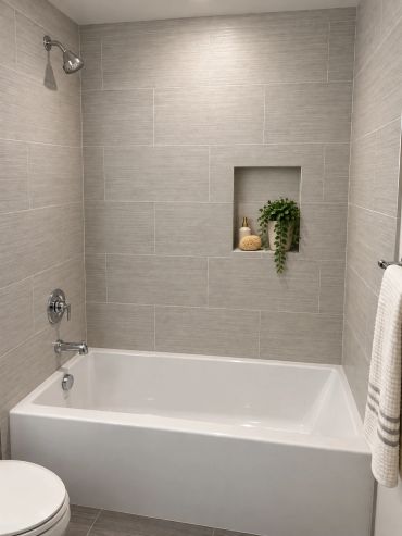 Modern bathtub with gray tiled walls and a plant.