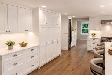 Modern white kitchen with wooden floor and bar stools.