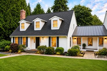 Charming white house with black roof and lush green lawn at dusk.