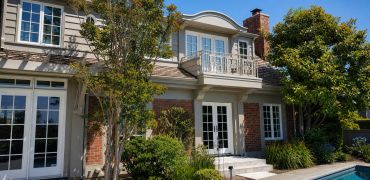 Elegant house exterior with white doors, brick walls, and lush greenery.
