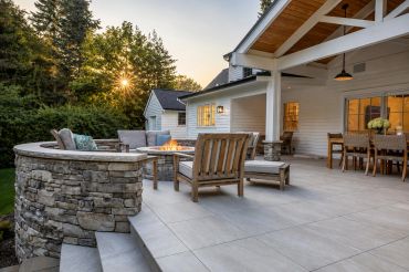 Elegant outdoor patio with stone fire pit and wooden furniture.