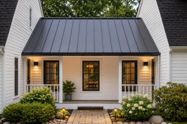 Modern white house porch with black metal roof and warm lights.