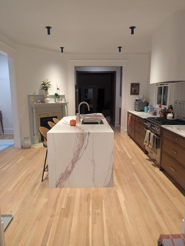 Modern, spotless kitchen with bright wood floors and a marble island, cleaned by Purely Home.