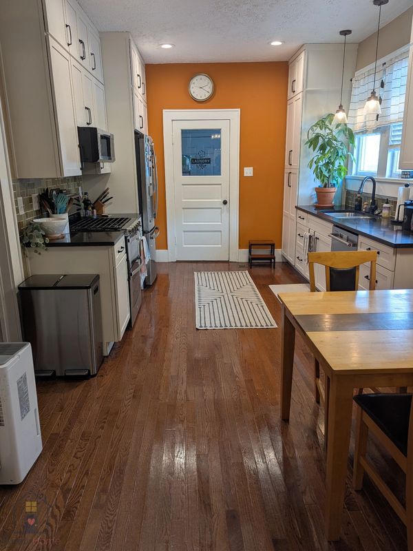 Bright, clean kitchen with white cabinets, hardwood floors, and orange accent wall.