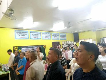 People gathered in a brightly lit room, engaged in singing or prayer.