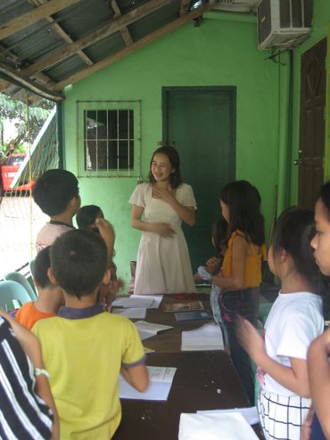 A woman teaches a group of children in a casual classroom setting.