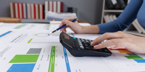 Person using calculator and pen to analyze financial charts and data.