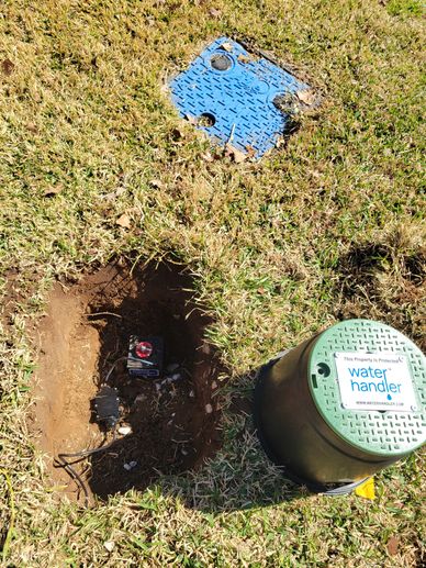 Water handler valve and opened ground in grassy area.