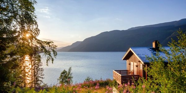 Cabin by a lake with mountains in the background at sunset.