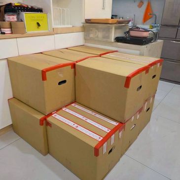 Stack of sealed cardboard boxes with red tape in a kitchen corner.