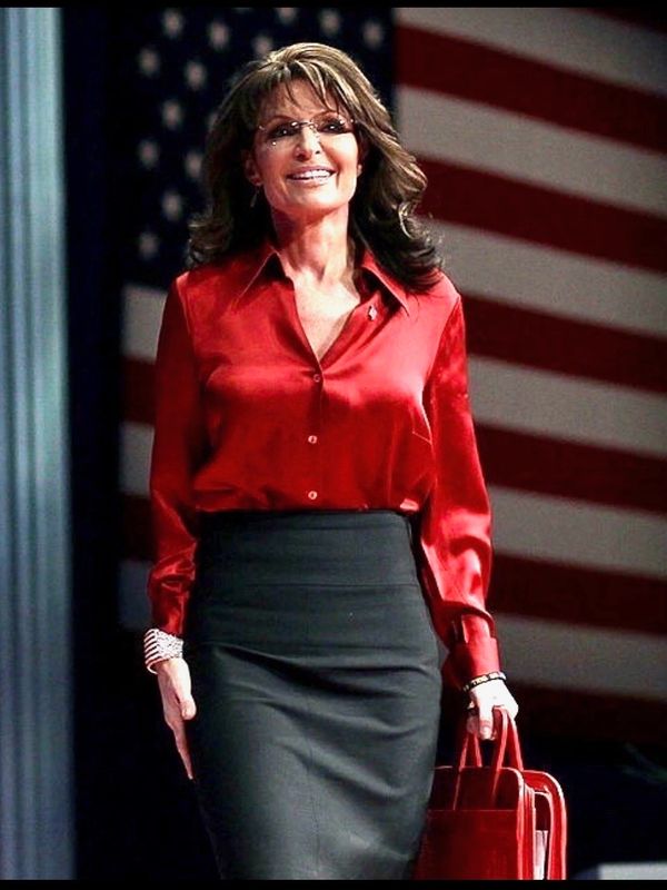 Woman in red blouse and black skirt standing in front of an American flag.
