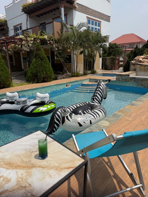 Inflatable zebra float in a pool near a blue chair and a green drink on a table.