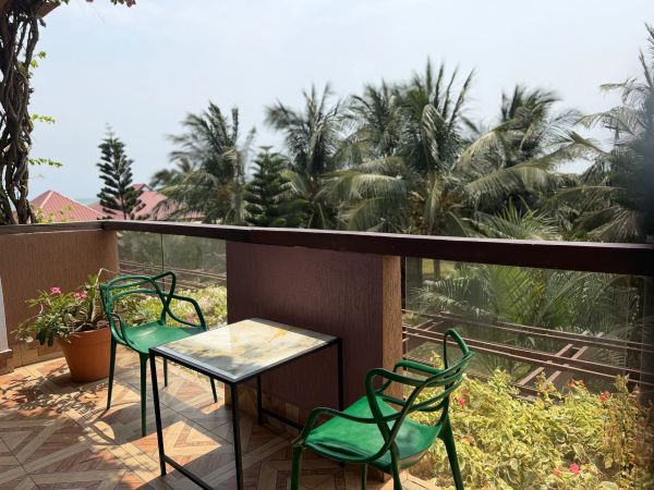 Balcony with green chairs, a small table, and tropical plants under a clear sky.