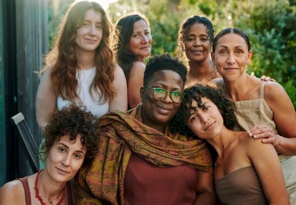 A diverse group of seven women posing outdoors with warm smiles.