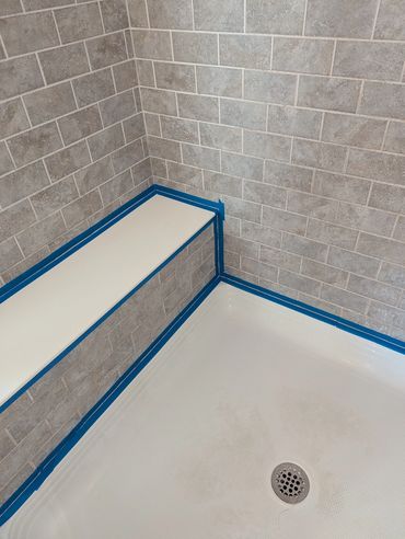 Shower corner with tiled walls, a bench, and blue painter's tape along edges.