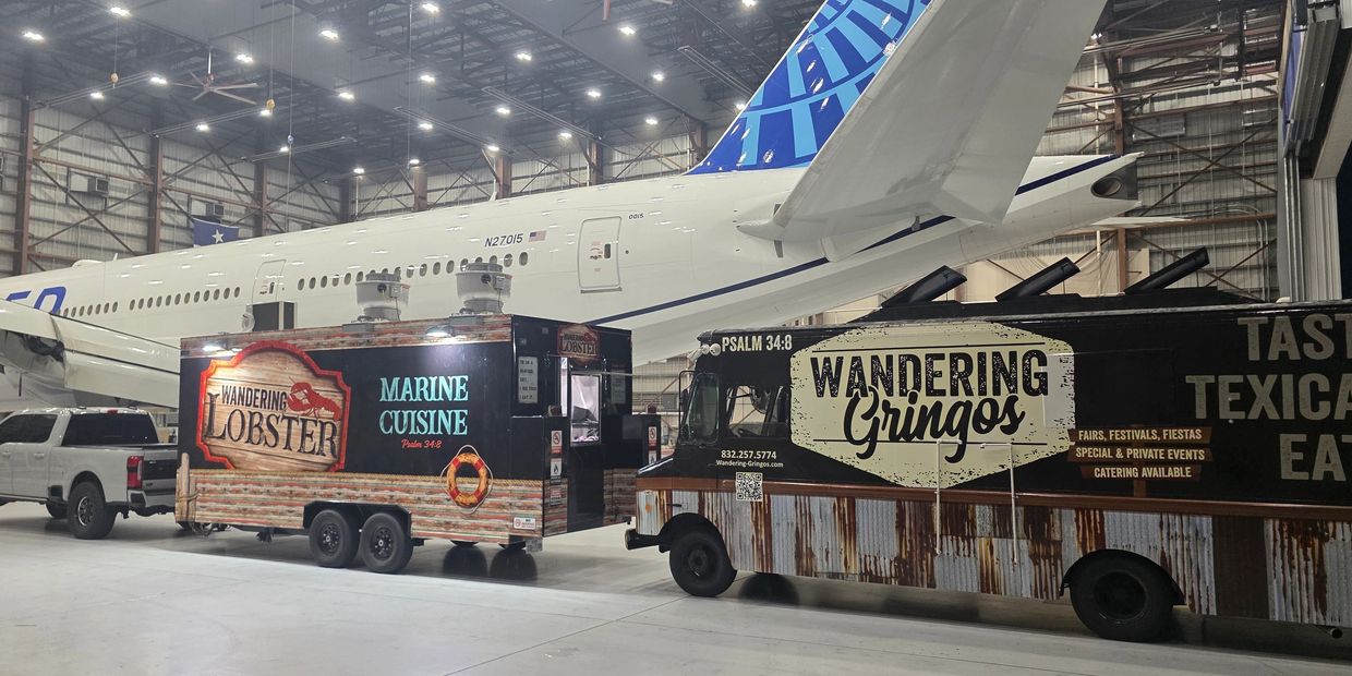 Two food trucks parked inside an airplane hangar beside a large aircraft.
