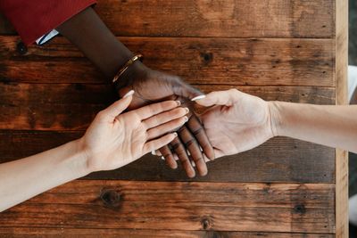 Hands of diverse people joined together on a wooden table.