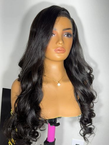 Mannequin head displaying long, wavy black hair with a side part and a delicate necklace.