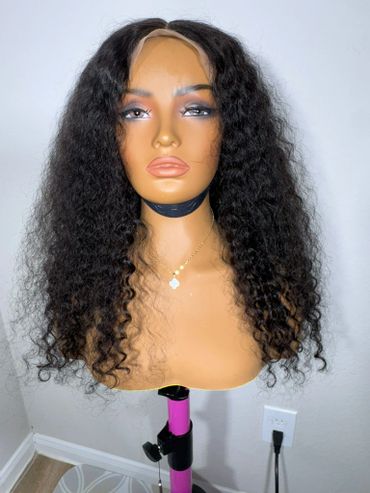Mannequin head with long curly black wig on a stand.