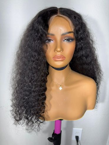 Curly black wig displayed on a mannequin head with makeup and necklace.