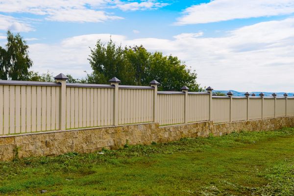 Long fence with a light-colored metal top and a stone base under a blue sky